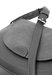Šedá kožená crossbody taška s sušenou klopou, nastavitelným popruhem, prošívanými detaily a koženým štítkem s logem. Jednoduchý, funkční design.