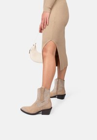 Botas de ante beige hasta el tobillo con acentos de malla metálica, punta cuadrada, tacón corto y detalle de cremallera lateral, combinadas con un vestido de punto acanalado.