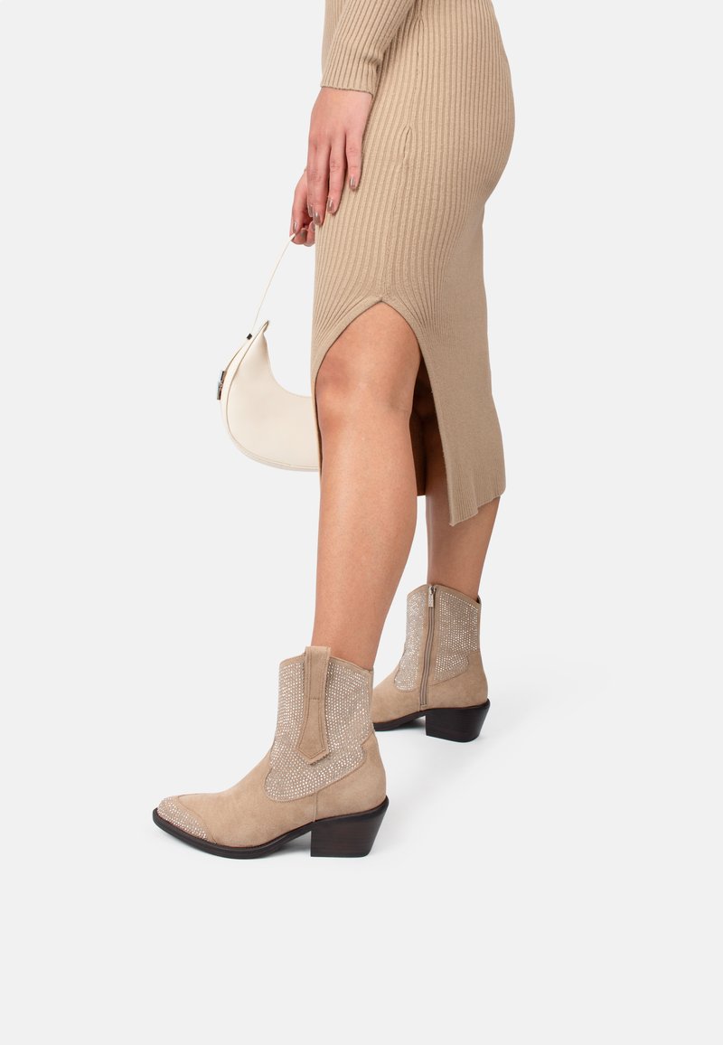 Botas de ante beige hasta el tobillo con acentos de malla metálica, punta cuadrada, tacón corto y detalle de cremallera lateral, combinadas con un vestido de punto acanalado.