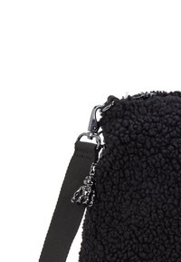Black fuzzy fabric bag with a textured surface, featuring a silver hardware clip and a black charm shaped like a character. Adjustable strap included.
