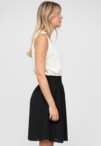 Jupe noire avec taille élastique, associée à un top sans manches blanc. Design simple, texture lisse et ajustement naturel.