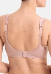 Soutien-gorge sans fil en tissu rose pâle doux. Il dispose de bretelles ajustables, d'une bande arrière lisse et d'un système de fermeture à crochets. Design épuré avec un matériel minimal.