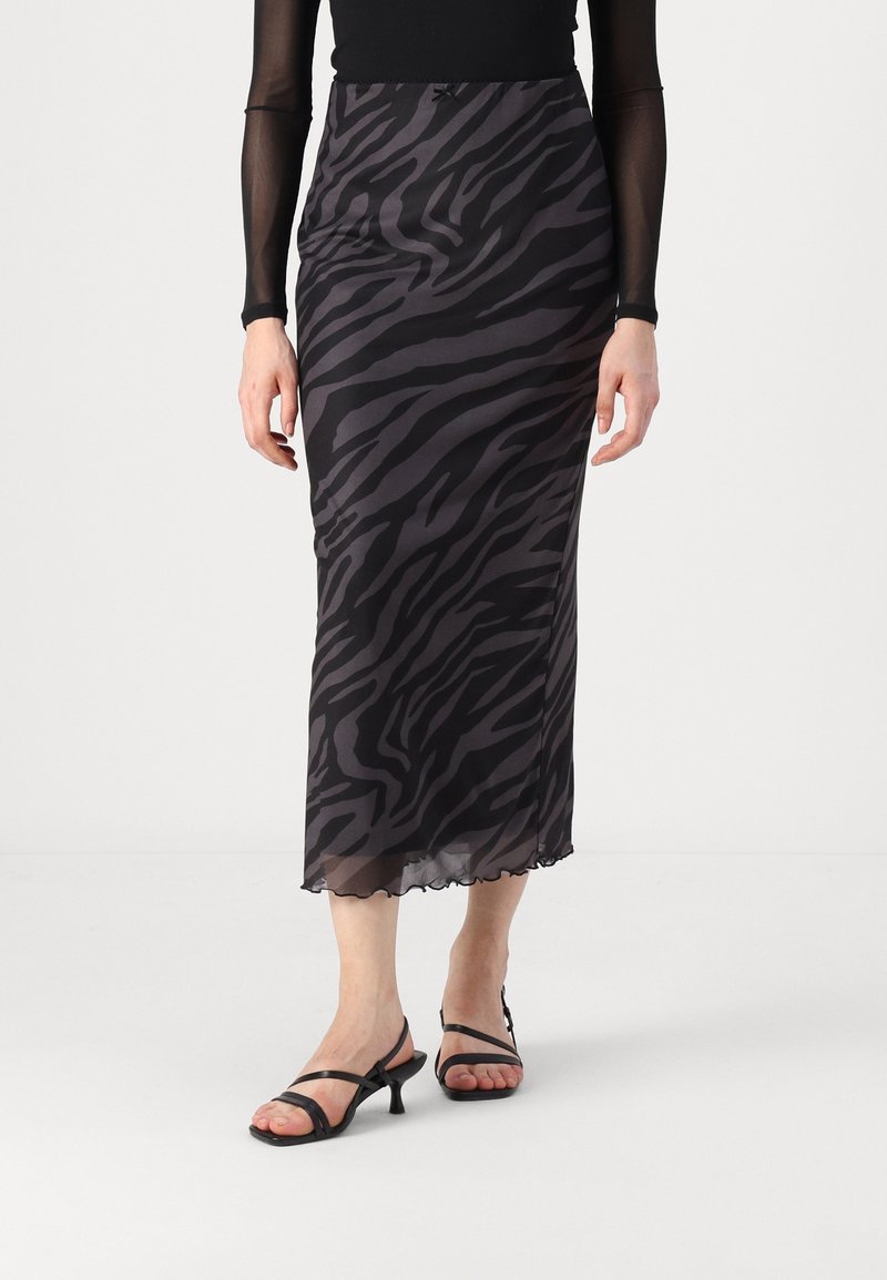 Jupe maxi en tissu noir transparent avec un imprimé zèbre gris. Dotée d'un ourlet festonné et d'une taille ajustée. Associée à des sandales noires à lanières.