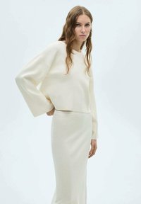 Pull en tricot couleur crème à manches longues, accompagné d'une jupe midi assortie. Les deux pièces ont une texture douce et une coupe décontractée.