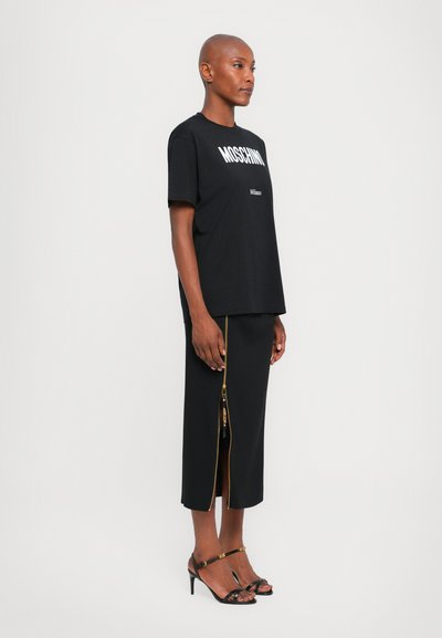 T-shirt noir avec le texte blanc "MOSCHINO Milano", associé à une jupe noire avec un détail zip doré sur le côté. Talons aiguilles noirs avec brides.