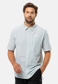 Lichtblauw kortemouwenshirt met een button-down kraag, textuurstof en een borstzak met een logo. Draag met donkere broeken.