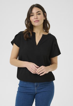 Sort kortærmet top med struktureret stof, en subtil V-hals og en løs pasform. Kombineret med blå denim jeans.
