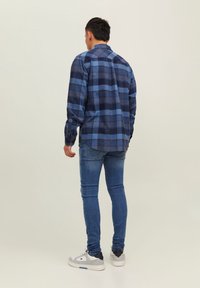 Camisa de cuadros azul de manga larga con un corte relajado; presenta tonos de azul oscuro y claro y un cuello clásico. Combinada con jeans ajustados azules.