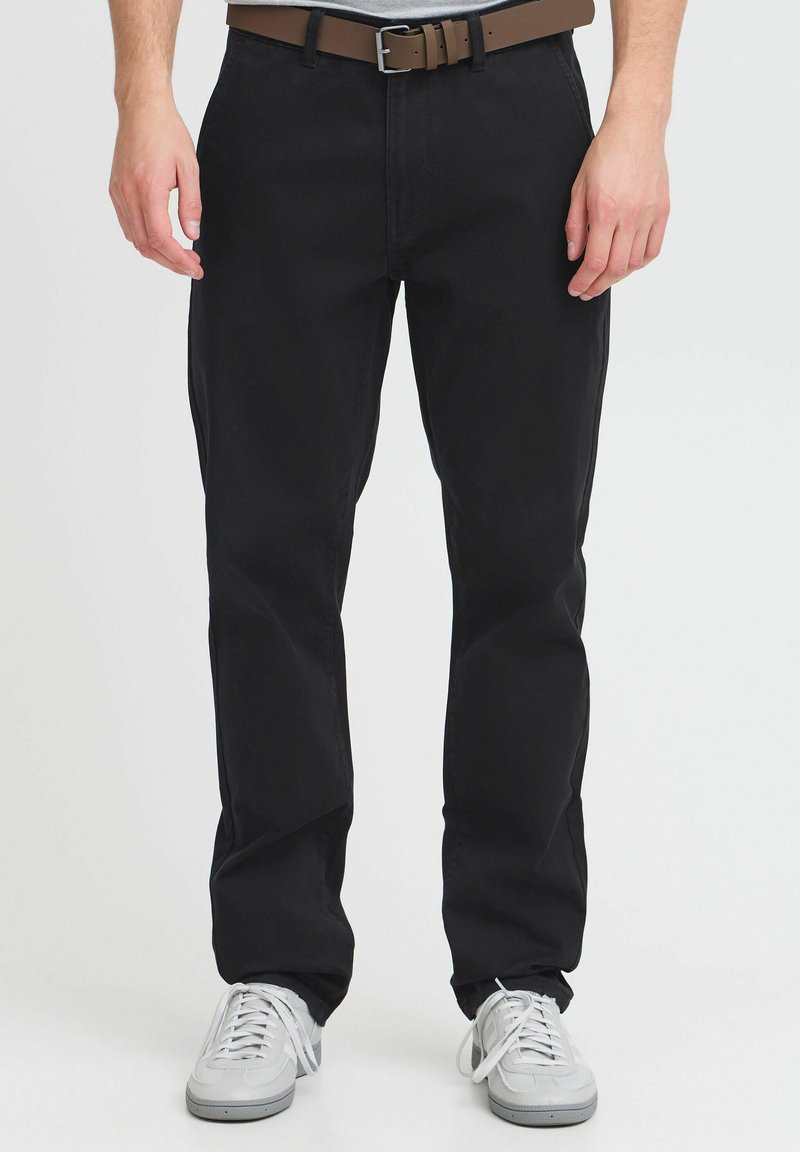 Pantalons en coton noir avec une coupe droite, accompagnés d'une ceinture en cuir marron et de baskets blanches. Texture lisse, design minimaliste et sans motifs visibles.