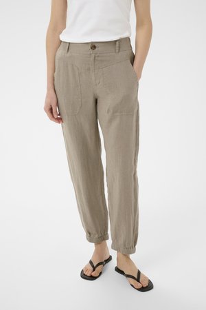 Person wearing beige casual pants with patch pockets and elastic cuffs, paired with black flip-flops and a white sleeveless top.