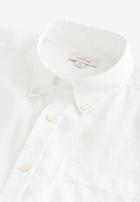 Camicia di lino bianca con colletto button-down, tasca frontale e quattro bottoni gialli. Etichetta con la scritta "NEXT SIGNATURE," taglia M.
