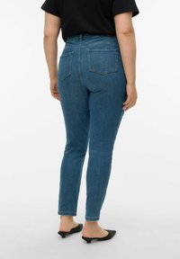 Kõrge vöökohaga sinised teksapüksid, millel on vormis siluett, viie tasku disain ja sile teksakangas. Tagatasku detailidega.