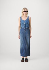 Jeans obleka z oprijetim zgornjim delom, zapiranjem na gumbe in dolgim krilom. Tkanina je srednje modra, z rahlim bledenjem. Črne čevlje z odprtimi prsti.