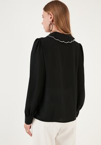 Black blouse with a scalloped collar and long puff sleeves, featuring a smooth texture. The back is plain with no visible fastenings.