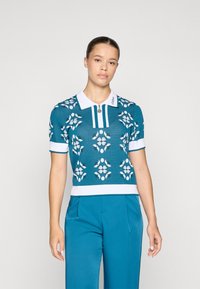 Strikket poloskjorte i teal med hvite blomster mønstre, korte ermer, ribbestrikket kant og krage med glidelåsdetalj og logo aksent.