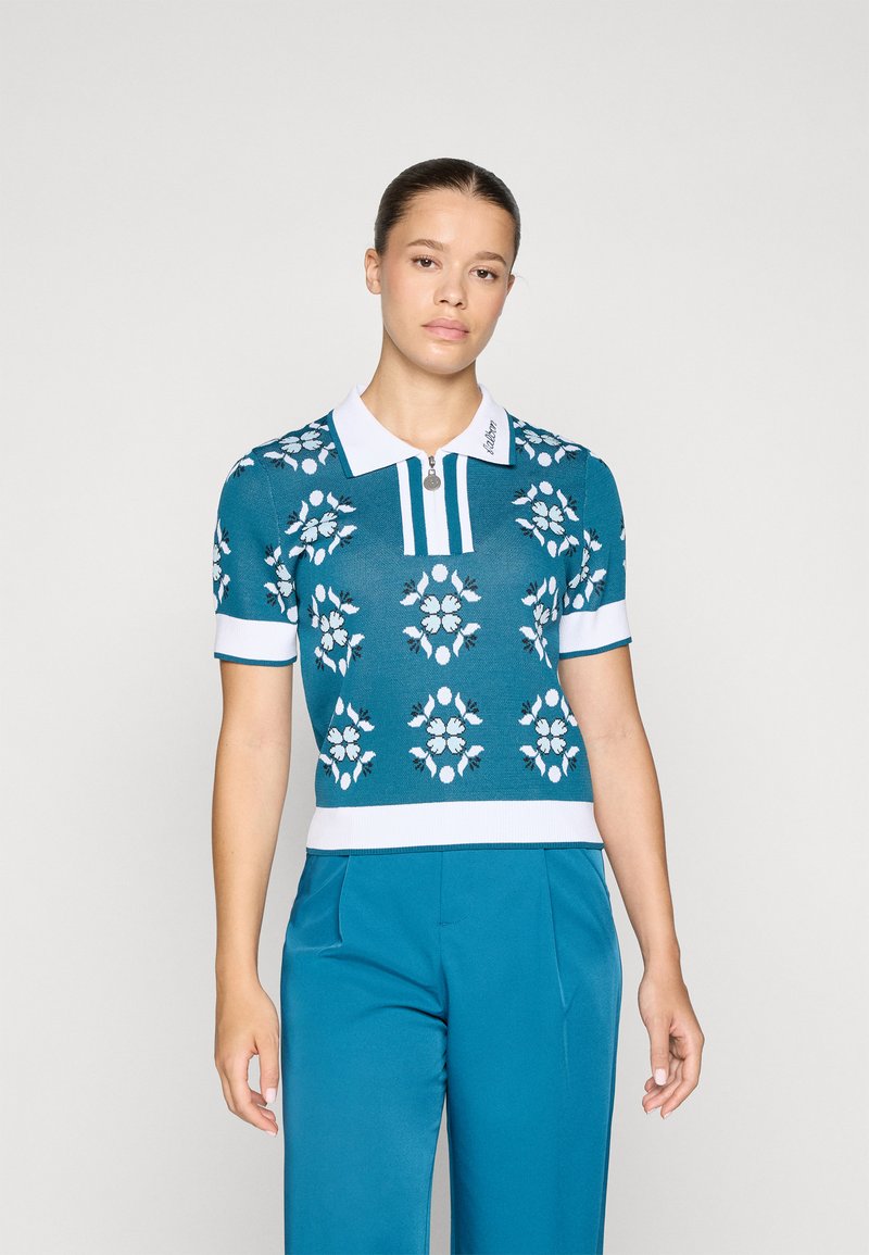 Strikket poloskjorte i teal med hvite blomster mønstre, korte ermer, ribbestrikket kant og krage med glidelåsdetalj og logo aksent.
