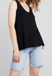 Haut noir sans manches avec un décolleté en V profond, fabriqué en tissu doux. Associé à un short en denim bleu clair avec une coupe décontractée arrivant au genou.