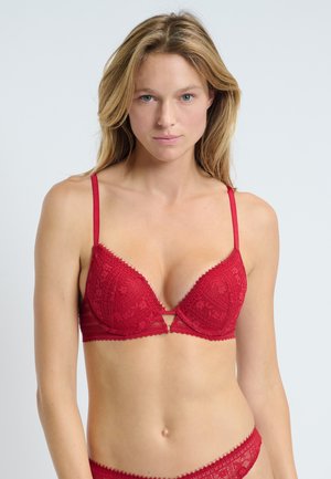 Soutien-gorge en dentelle rouge avec une forme triangulaire, fines bretelles ajustables, détail en découpe en forme de clé au centre et bords festonnés le long des bonnets.