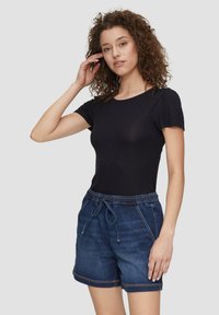 Schwarzes, kurzärmeliges, tailliertes Oberteil, kombiniert mit dunkelblauen Jeans-Shorts mit elastischem Bund und Kordelzug, die Seitentaschen und sichtbare Nähte aufweisen.