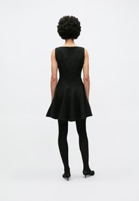 Μαύρο φόρεμα σε σχήμα Α με αμάνικη σχεδίαση  και στρογγυλή λαιμόκοψη. Διαθέτει εφαρμοστό μπούστο, φουσκωτή φούστα και κλείσιμο με φερμουάρ στο πίσω μέρος.