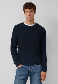 Marineblauer gerippter Pullover mit langen Ärmeln und Rundhalsausschnitt, kombiniert mit blauen Jeans. Verfügt über einen weißen Innenkragen und ein minimalistisches Design.