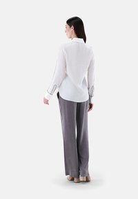 White button-up shirt with black accents, paired with gray wide-leg pants. The fabric appears soft and lightweight, enhancing overall flow.