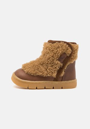 Brown toddler boots featuring a soft, tan shearling upper, leather accents, a rounded toe, and a rubber sole with textured grip patterns.