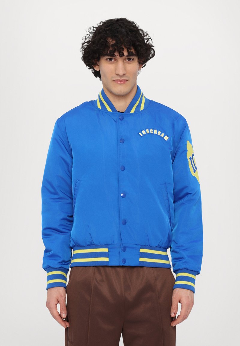 Cazadora bomber azul con cuello y puños de canalé a rayas amarillas y verdes. Logo "ICECREAM" bordado en el pecho; tejido texturizado; botones a presión.