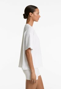 Tricou alb oversized cu mânecă scurtă, cu decolteu rotund, fabricat dintr-un material moale, având o croială lejeră și cusături laterale accentuate.