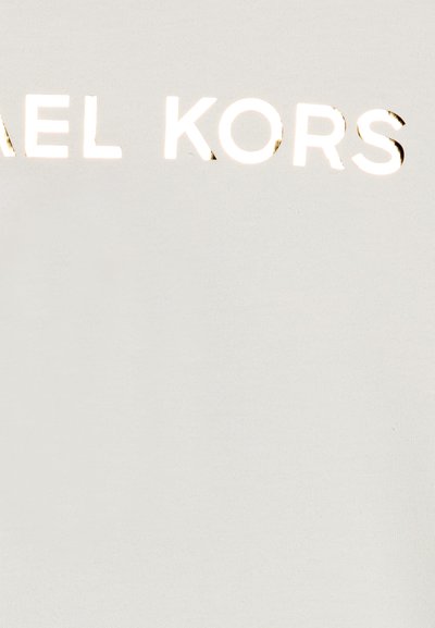 Vue partielle d'un tissu blanc avec des lettres réfléchissantes en argent épelant "EL KORS" en haut au centre.