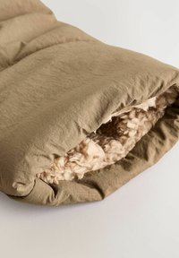 Olivgrön vadderad ytterlager med en texturerad, fluffig beige foder. Tyget verkar mjukt och något skrynkligt, vilket visar en mysig design.