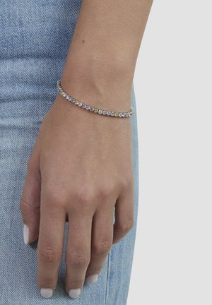 Primo piano di una mano che indossa un braccialetto d'argento con pietre preziose dai colori pastello alternati, appoggiata su jeans di denim azzurro chiaro.