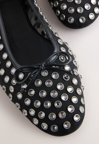 Ballerines en tissu noir ornées de multiples strass argentés et transparents, avec un nœud décoratif à l'avant et une doublure intérieure lisse.