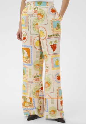 Krémové nohavice s širokými nohavicami s farebnými rámovanými potlačami ovocia vrátane čerešní, hrozna, ananásu, pomaranča, citróna a melónu, nosené s čiernou obuvou.