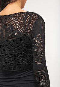 Black garment with a textured knit design featuring intricate patterns on the sleeves and a smooth lower section.