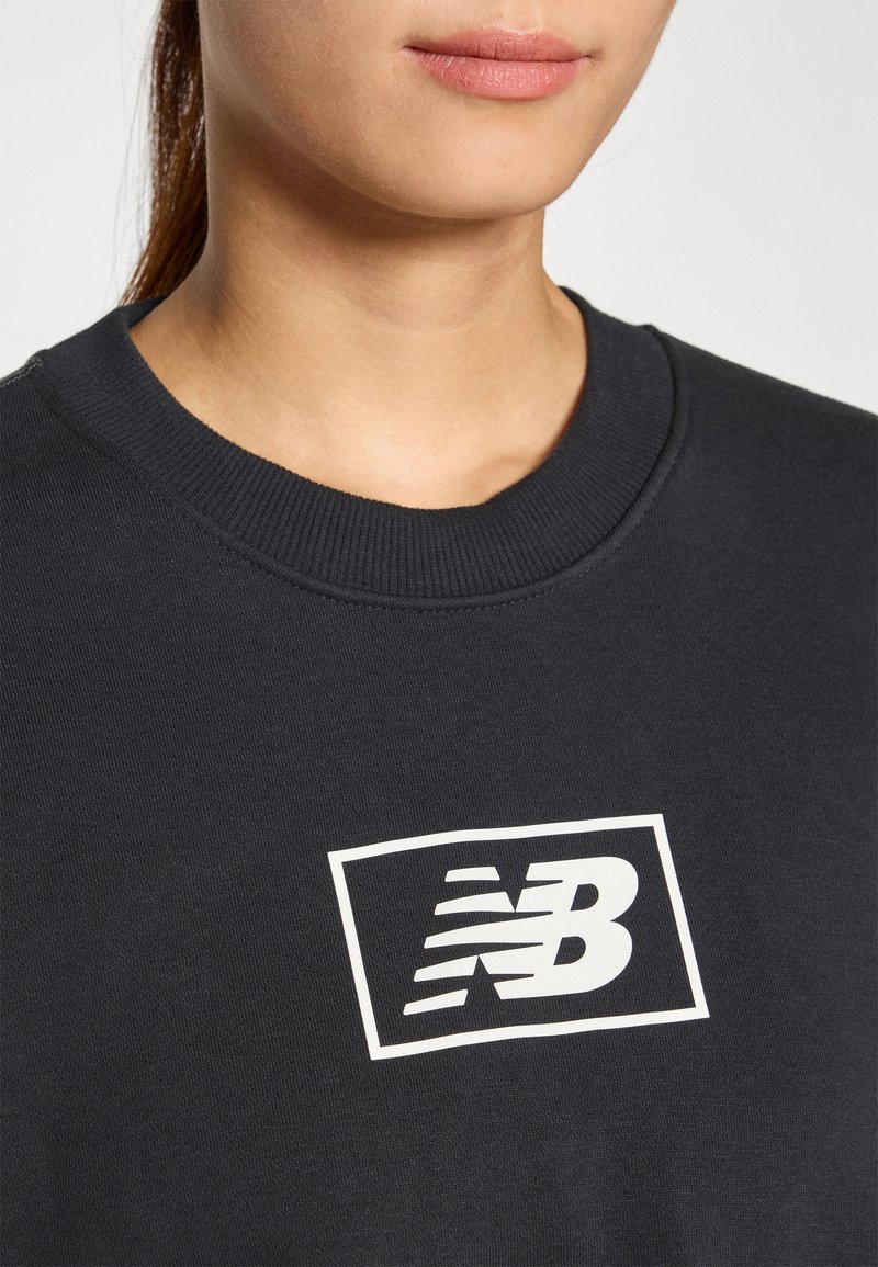 Felpa nera con colletto a costine, caratterizzata da un grande logo New Balance bianco racchiuso in un contorno rettangolare. Tessuto morbido.