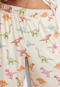 Katoenen pyjamashorts met een crèmekleurige achtergrond en meerkleurige dinosaurustrends in oranje, roze, groen en blauw. Elastische tailleband.