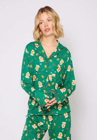 Ensemble de pyjama vert arborant un motif de maison en pain d'épice avec des accents rouges. Tissu doux et design à boutons avec des manches longues et des poches.