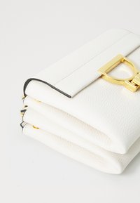 Balta ādas clutch soma ar akmens struktūru, kurai ir zelta tonēta aizdare un kontrastējoši melni malu akcenti. Redzams saliekts dizains.