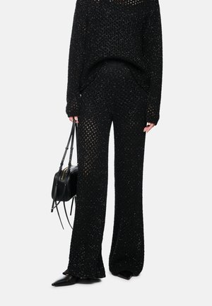 Woman wearing black knitted wide-leg pants and matching sweater, holding a black handbag, with black pointed shoes.