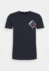 Camiseta de algodón azul marino con un diseño gráfico en el lado izquierdo del pecho que incluye texto y formas en blanco y rojo. Mangas cortas y cuello redondo.