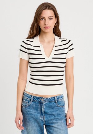 Top polo bianco a maniche corte con righe orizzontali nere, scollatura a V e texture a coste, abbinato a jeans blu a vita alta.