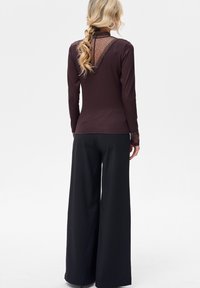 Czekoladowobrązowa koszula z długim rękawem z koronkowym tyłem, zestawiona z czarnymi spodniami o szerokich nogawkach, tworząca kontrast warstwowej tekstury.