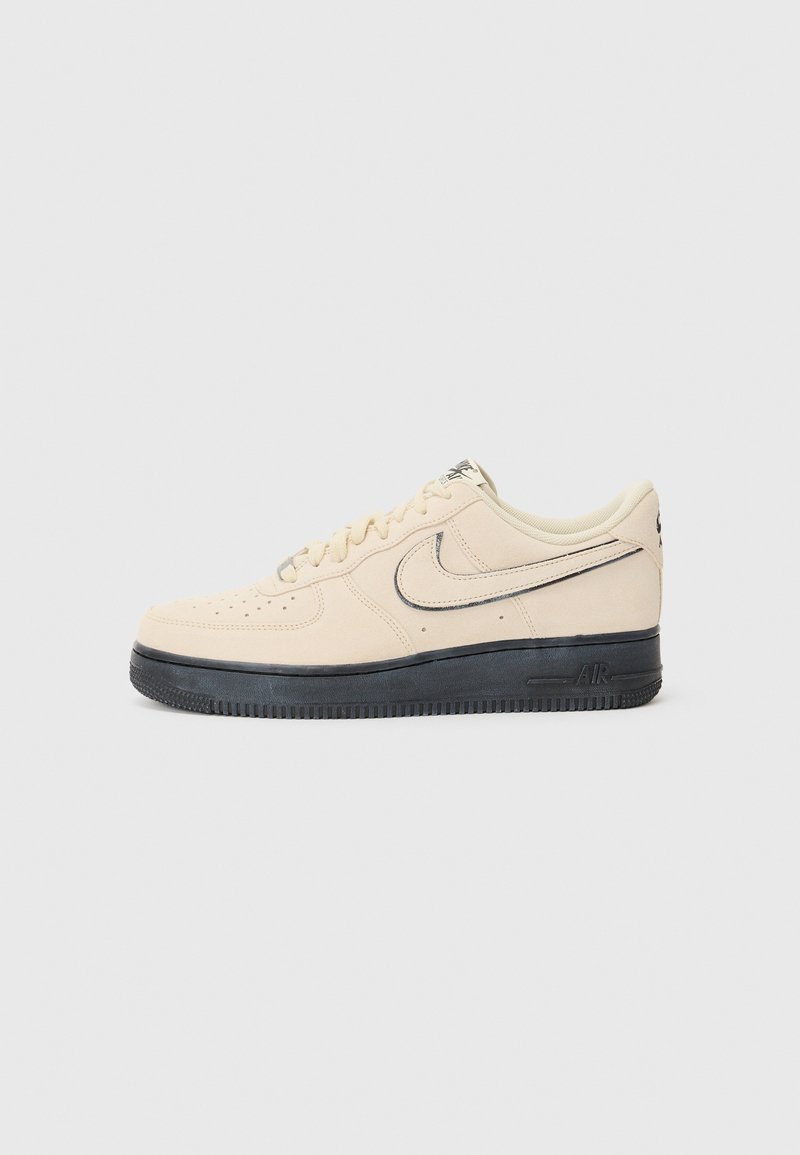 Beige südamega Nike Air Force 1 tossud musta kummitallaga, õmmeldud aktsendid, aukudega varvas ja silmapaistev swoosh logo.