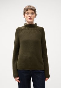Maglione lavorato a maglia verde oliva con colletto alto, maniche lunghe e vestibilità comoda. Presenta una texture a coste e un design con maniche raglan.