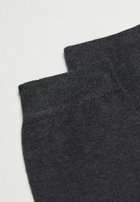 Calcetines de lana negros con una textura suave, con un puño acanalado y un diseño de punta sin costuras, dispuestos planos sobre un fondo liso.