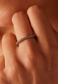 Zilveren ring met een gemêleerd patroon om een vinger, met een smalle, gladde band en een gedetailleerd oppervlakontwerp. Huidtextuur zichtbaar op de achtergrond.