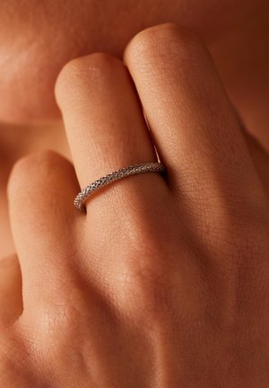 Zilveren ring met een gemêleerd patroon om een vinger, met een smalle, gladde band en een gedetailleerd oppervlakontwerp. Huidtextuur zichtbaar op de achtergrond.