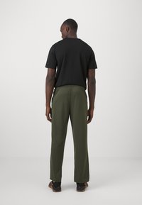 Sort kortærmet t-shirt med rund halsudskæring, parret med olivengrønne bukser med elastisk talje. Modellen står med ryggen til betrakteren.
