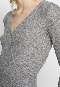 T-shirt en tricot ribbé gris avec un décolleté en V profond, une coupe ajustée et un tissu texturé. Les manches sont ajustées, mettant en valeur la forme du vêtement.